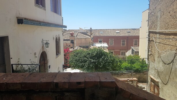 Ein schmaler Gang mit traditioneller Architektur, darunter ein weißes Gebäude mit Balkon und ein rotes Gebäude mit Ziegeldach.