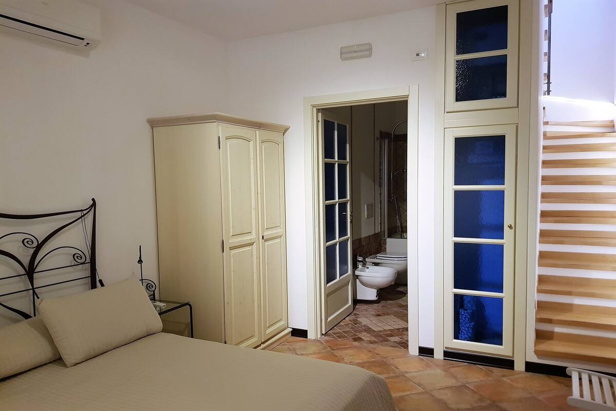 Een slaapkamer met een bed, een kledingkast en een badkamer, zichtbaar door een geopende deur.