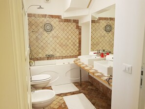 Een badkamer met een bad, twee wasbakken, een toilet en een douche.