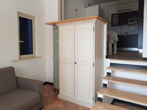 Een kamer met een grijze bank, een witte kast en een keuken met een magnetron en kastjes.