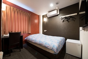 A hotel room with a bed, a desk, a chair, an air conditioning unit, and a small refrigerator. - Otsuka Town Hotel 24 (Tokyo)