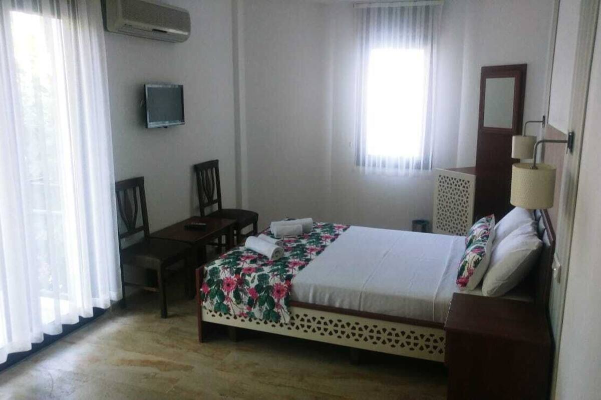 Een hotelkamer met een bed, een bureau, een stoel, een televisie en een raam met gordijnen.