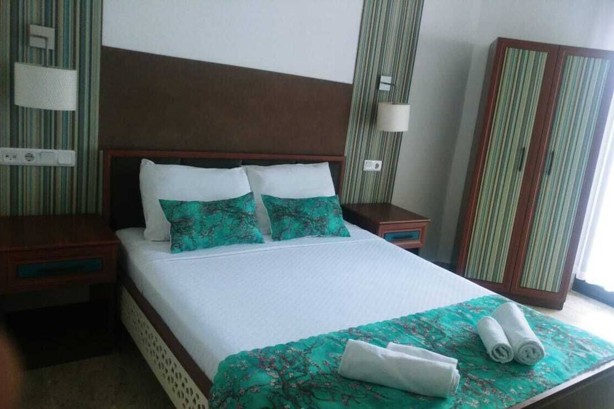 Een hotelkamer met een bed, twee nachtkastjes, een kledingkast en een raam met gordijnen.