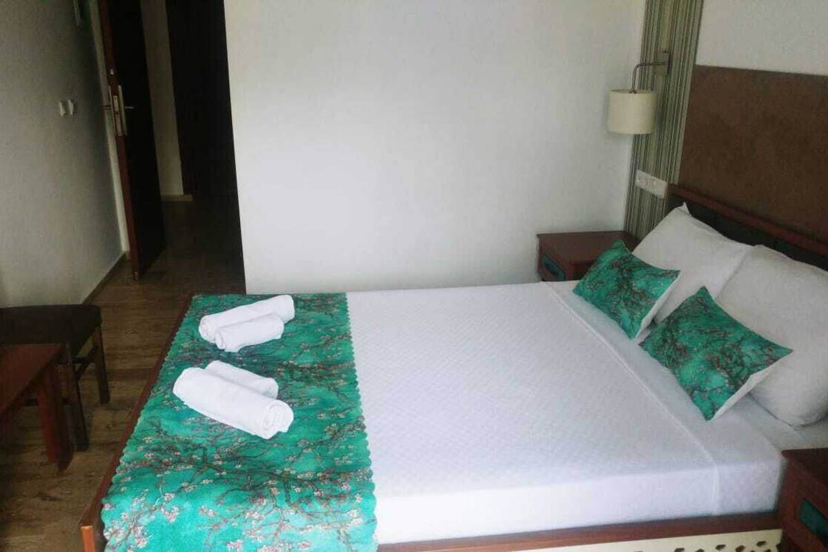 Een netjes opgemaakt bed met groen-witte beddengoed, twee kussens en twee opgerolde handdoeken op het bed.