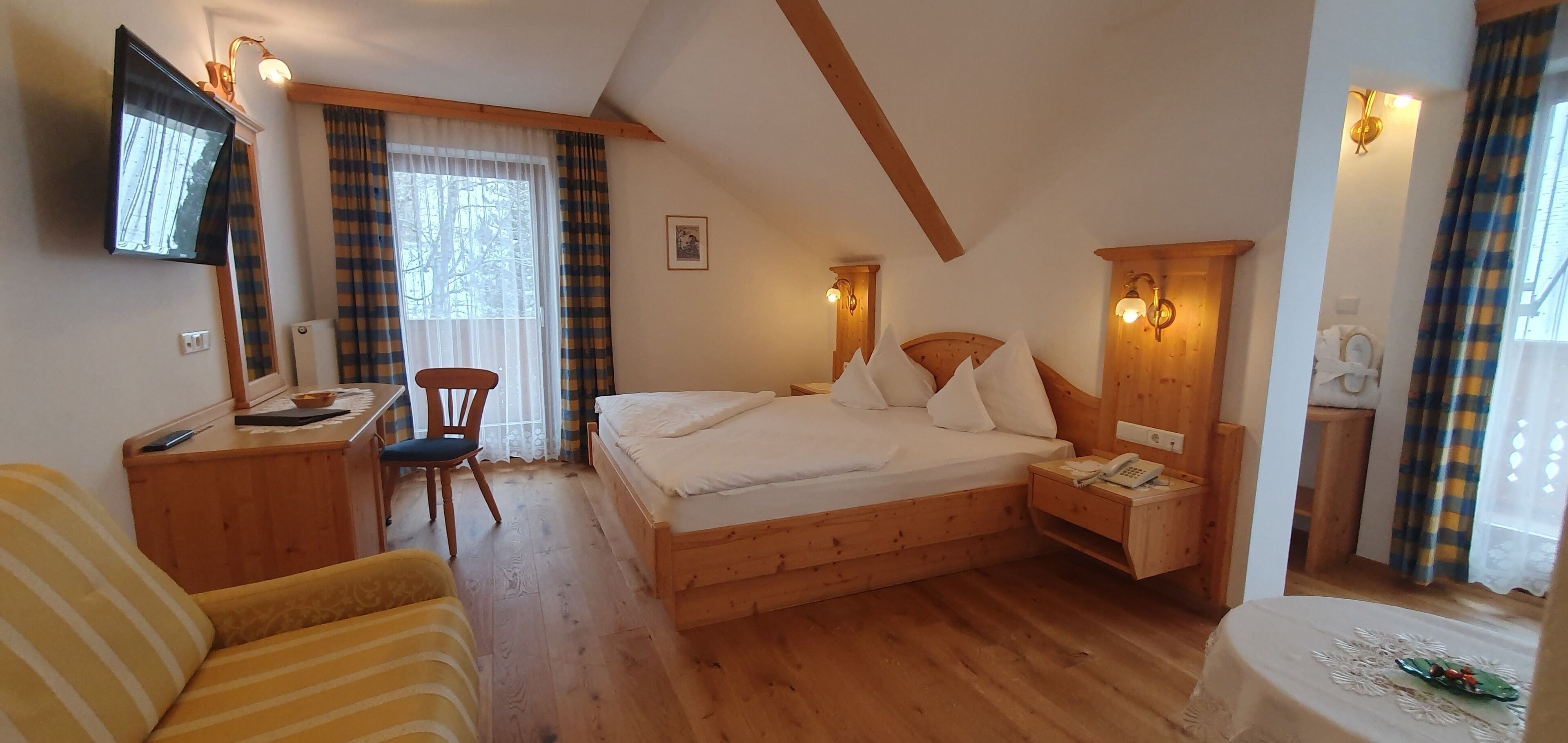 Ein Schlafzimmer mit einem hölzernen Bett, einem Schreibtisch, einem Stuhl und einem an der Wand befestigten Fernseher.