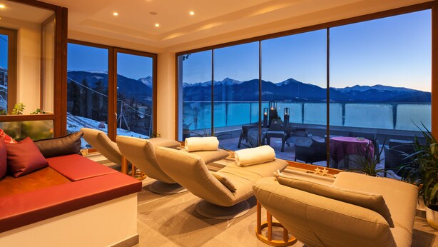 Un área de descanso moderna con ventanas amplias que dan a un lago y montañas.