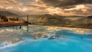 Una piscina con barrera de vidrio, rodeada de montañas y un cielo nublado.