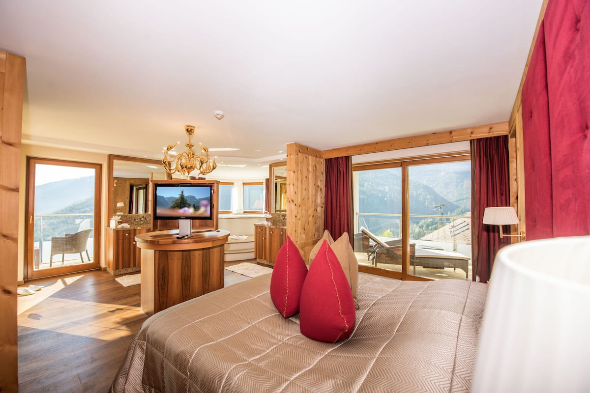 A spacious bedroom with a large bed, a television, and a balcony with a mountain view.