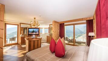 A spacious bedroom with a large bed, a television, and a balcony with a mountain view.