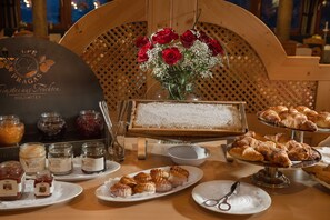 Una mesa con pasteles, mermeladas y un jarrón de rosas rojas.