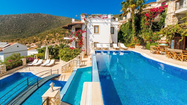 A swimming pool with lounge chairs and a view of a mountainous landscape. - Beautifully-located Large 2 bed, sea view garden apartment with shared lge pools (Kalkan)