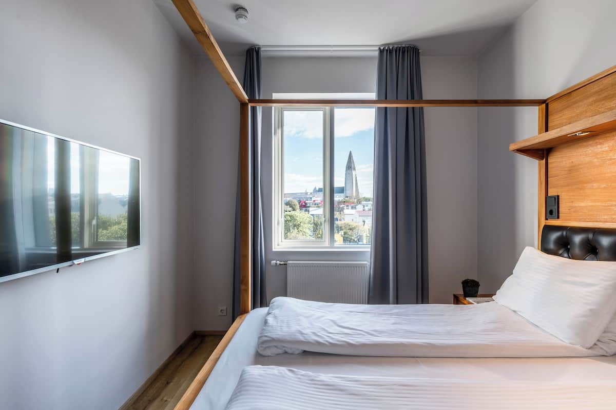 A modern hotel room with a large bed, a TV mounted on the wall, and a window with a view of a cityscape.