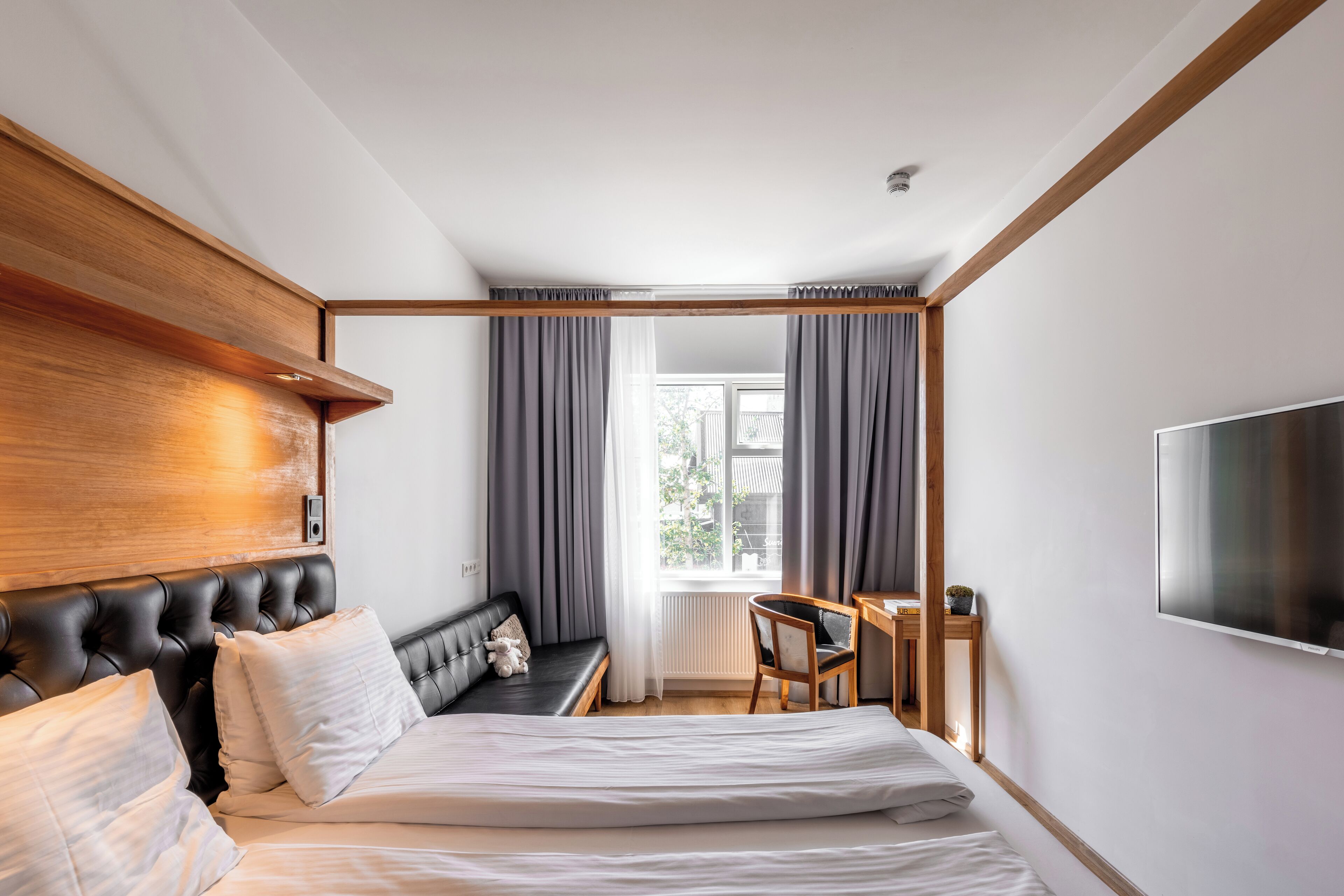 Un dormitorio moderno con una cama grande, cabecera de madera, un escritorio y un televisor.