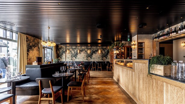 A restaurant with wooden flooring, a bar area with bottles, and a view of the street.