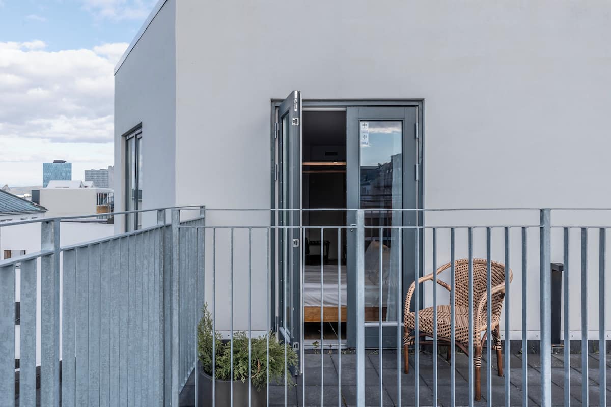 A balcony with a wicker chair, a bed, and a sliding glass door leading to an interior room.