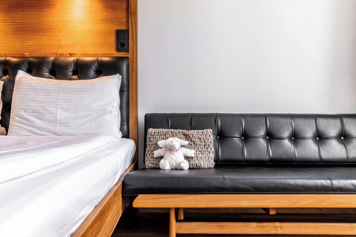 A bedroom with a bed, a black leather sofa, and a stuffed animal.