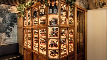 A wine cellar with multiple shelves of wine bottles, a wooden bench, and a wall with a floral pattern.