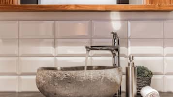 A stone basin sink with a modern faucet, a soap dispenser, and a rolled towel on a dark countertop.