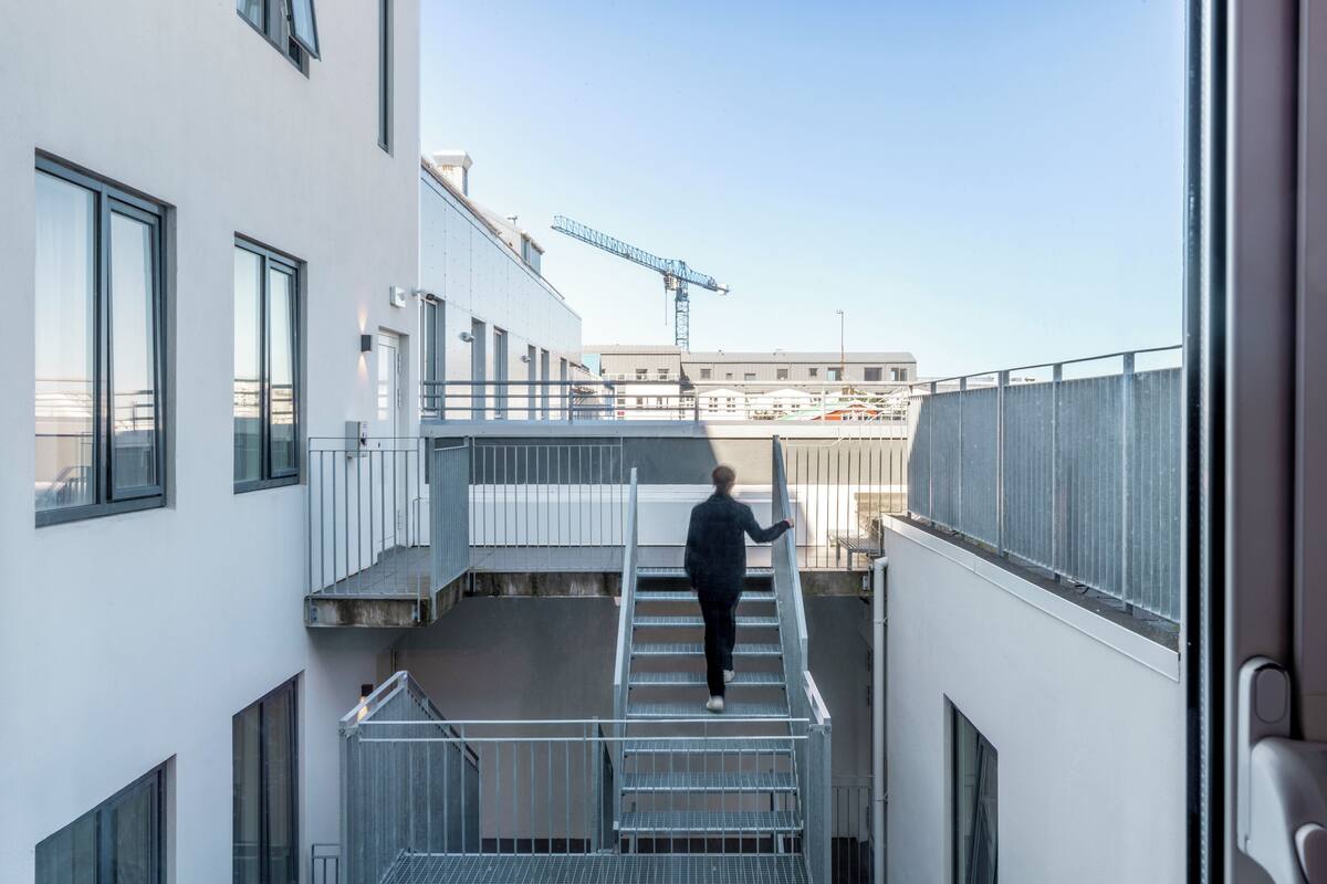 A person descending a metal staircase in a modern building with large windows and a construction crane in the background.