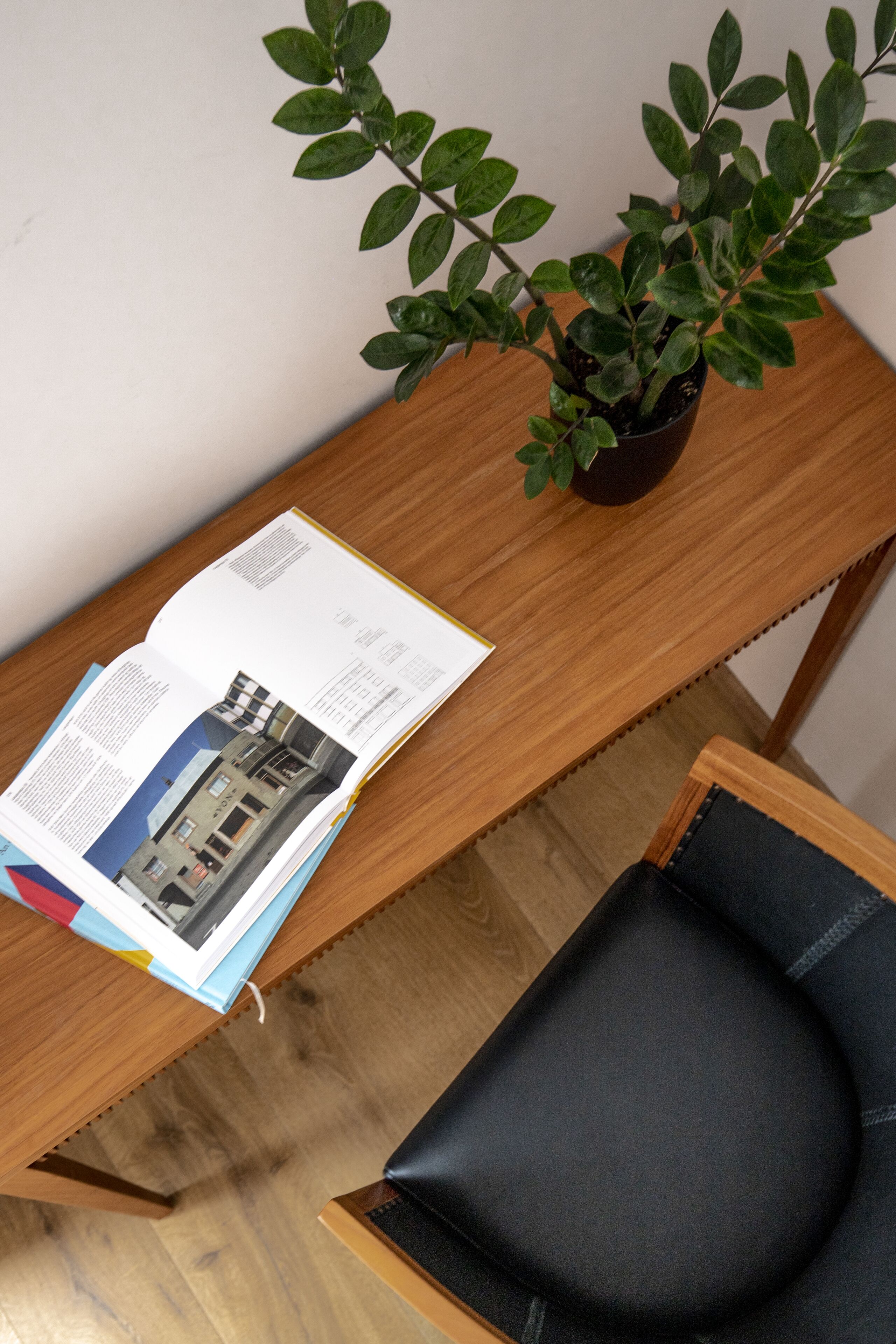 A wooden desk with a book, a potted plant, and a black chair.