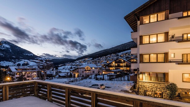 Un village de montagne enneigé, avec des bâtiments modernes et un balcon en bois.
