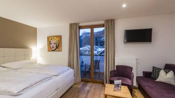 Hotelkamer met een bed, een stoel, een bank, een televisie en een raam met uitzicht op een besneeerd landschap.