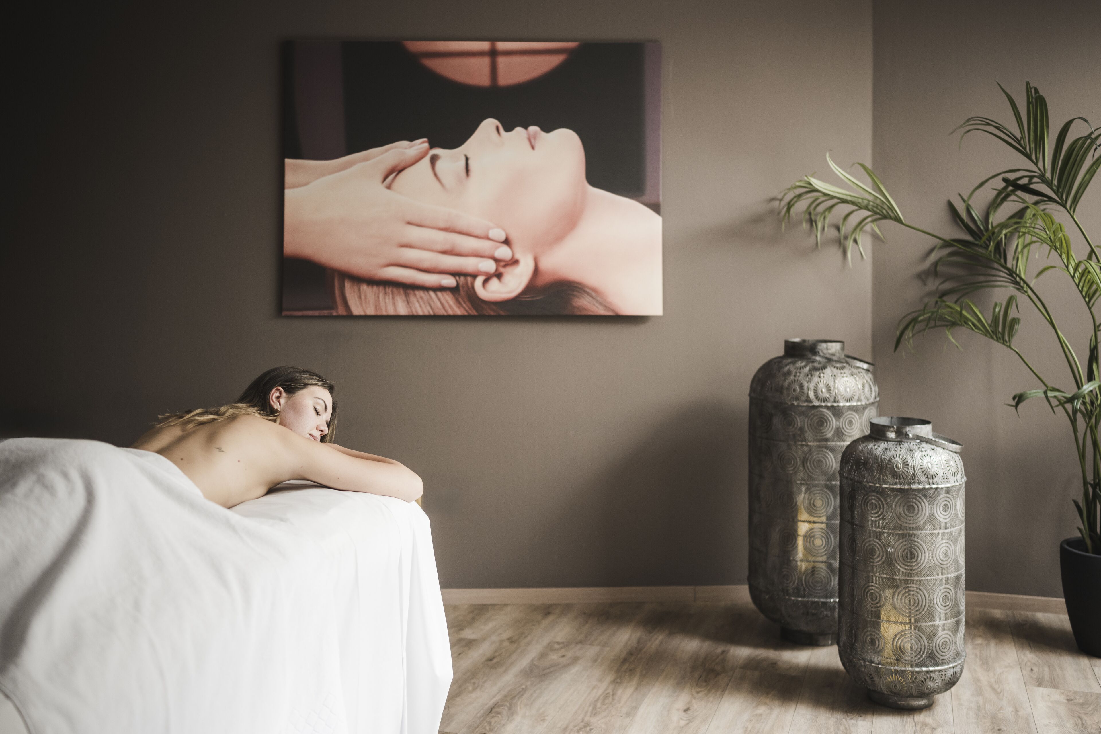 Une salle de spa équipée d’une table de massage, d’une grande œuvre d’art encadrée et de deux vases décoratifs en métal.