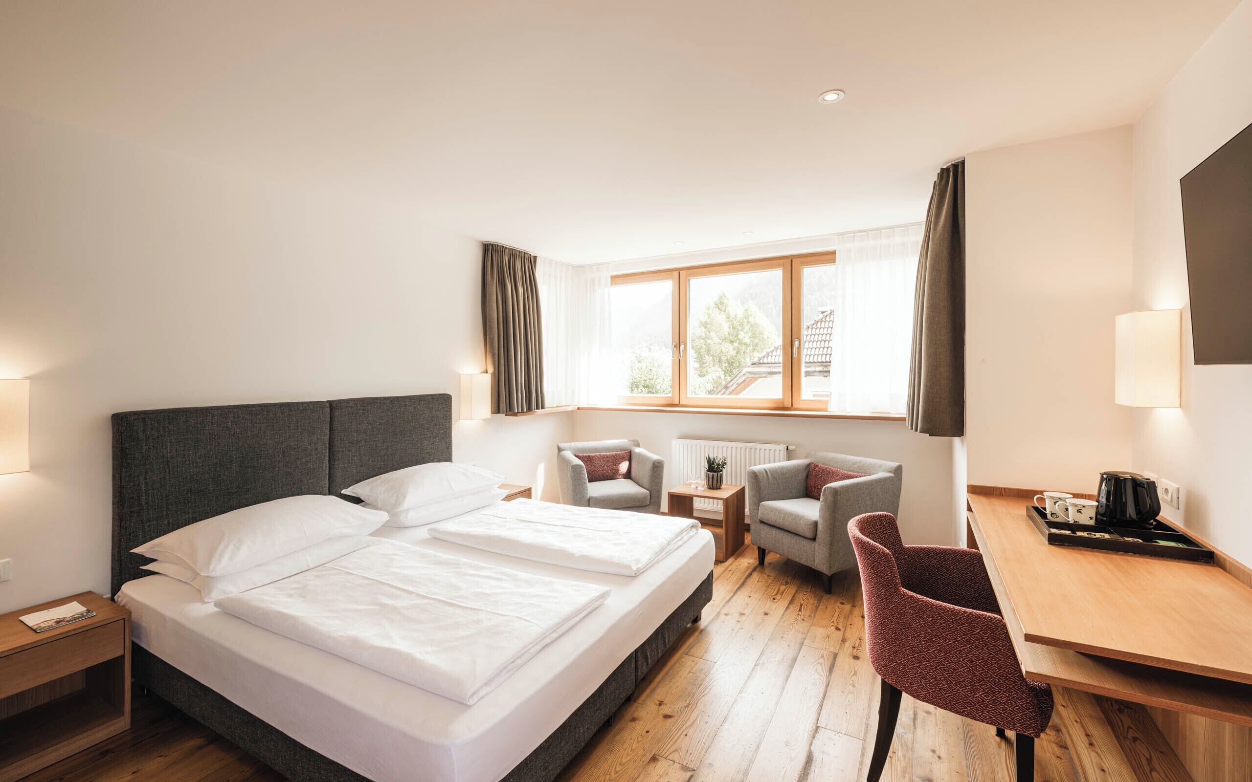 Una habitación de hotel con una cama grande, un escritorio, dos sillas, un televisor y una ventana con cortinas.