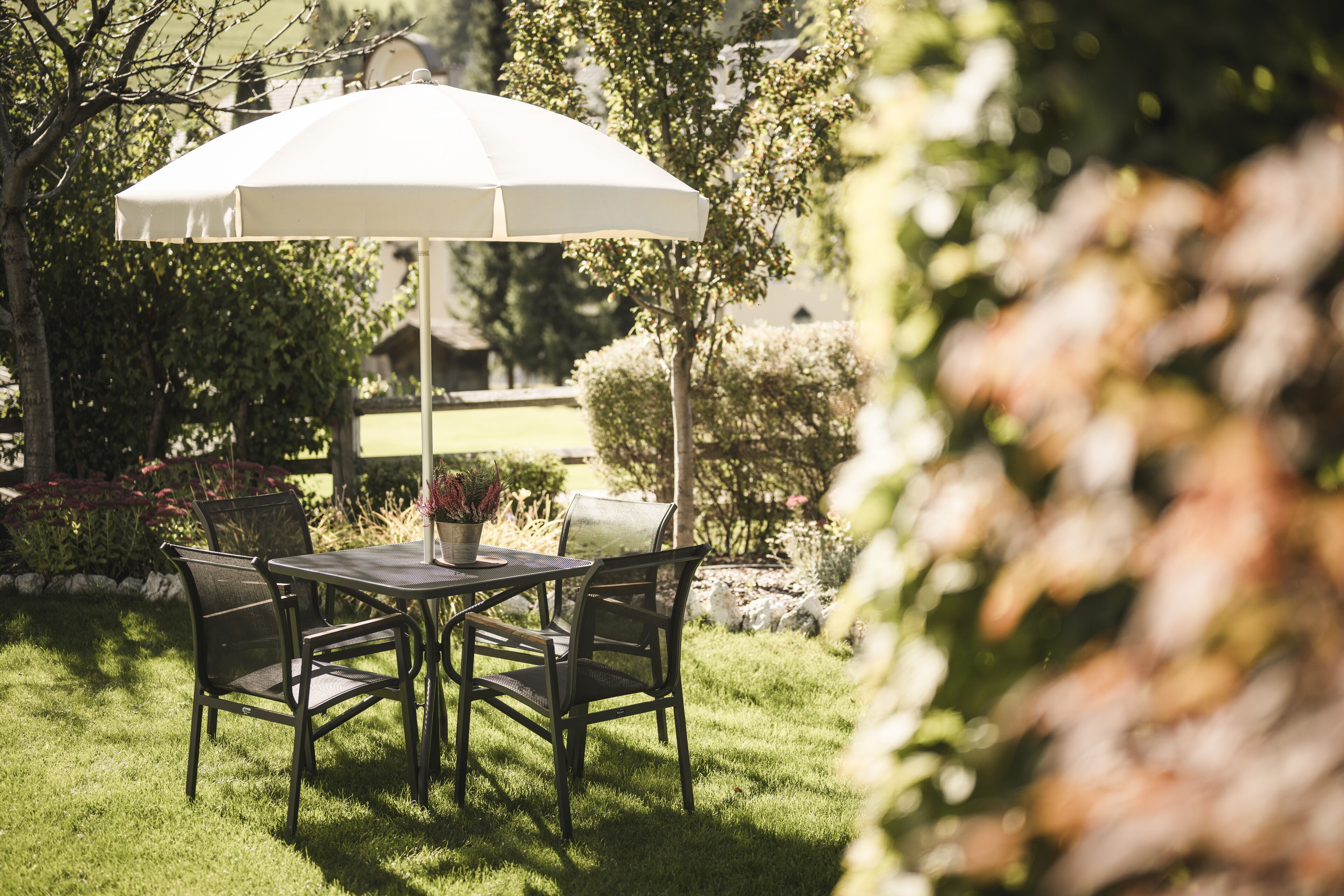 Eine Terrasse im Freien mit Tisch und Stühlen, einem weißen Sonnenschirm und einem Garten.