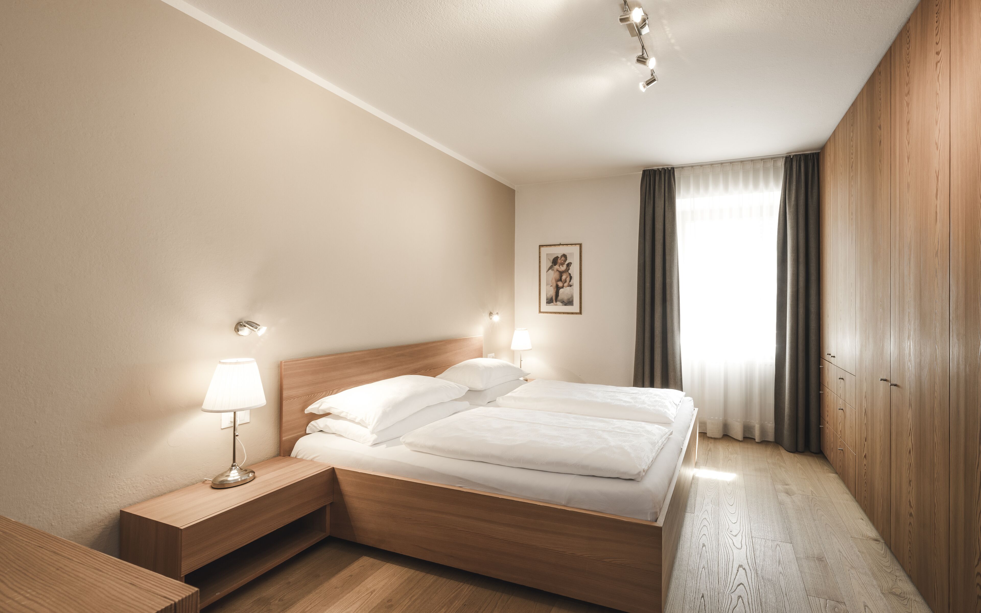 Ein Hotelzimmer mit einem hölzernen Bett, Nachttischlampen, einem Nachttisch, einem gerahmten Bild an der Wand und einem Kleiderschrank.
