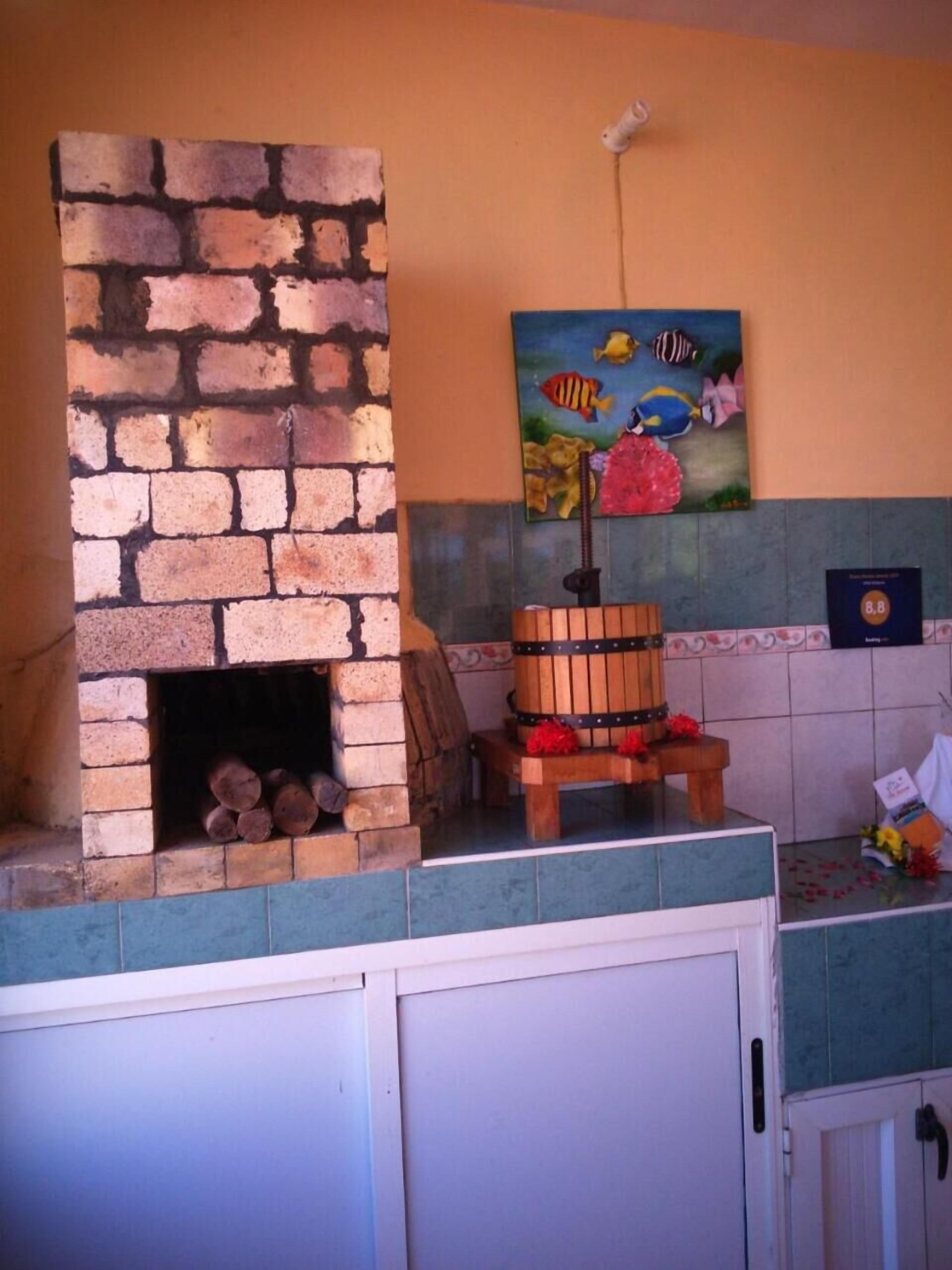 A kitchen with a brick oven, a wooden barrel, and a colorful fish painting on the wall.