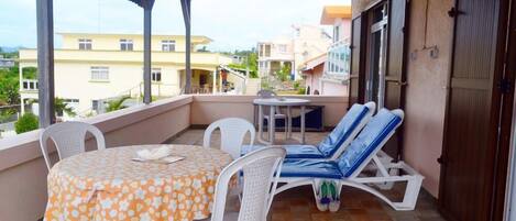 Un balcón con mesa y sillas, una silla de lounge y vistas de edificios circundantes.