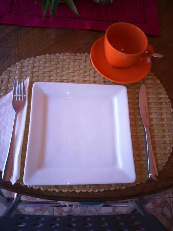 Una mesa con un plato blanco, un tenedor, un cuchillo y una taza y platillo naranja.