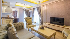 A modern living room with a sofa, armchair, coffee table, TV, and a kitchen area visible in the background. - Alanya Towers C Blok (Alanya)