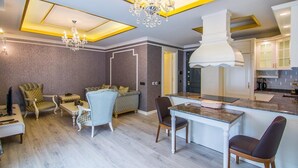 A modern kitchen with a central island, a dining area with a chandelier, and a living room with a sofa and chairs. - Alanya Towers C Blok (Alanya)