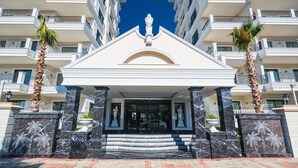 A hotel entrance with a white facade, marble steps, and palm trees. - Alanya Towers C Blok (Alanya)
