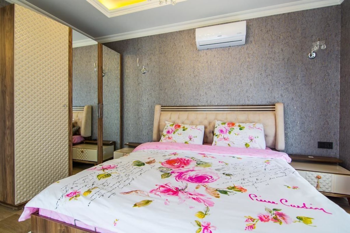 A bedroom with a bed, a nightstand, a mirror, and a wall-mounted air conditioner.