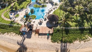 Luftaufnahme eines Resorts mit Schwimmbad, Strand und Palmen.