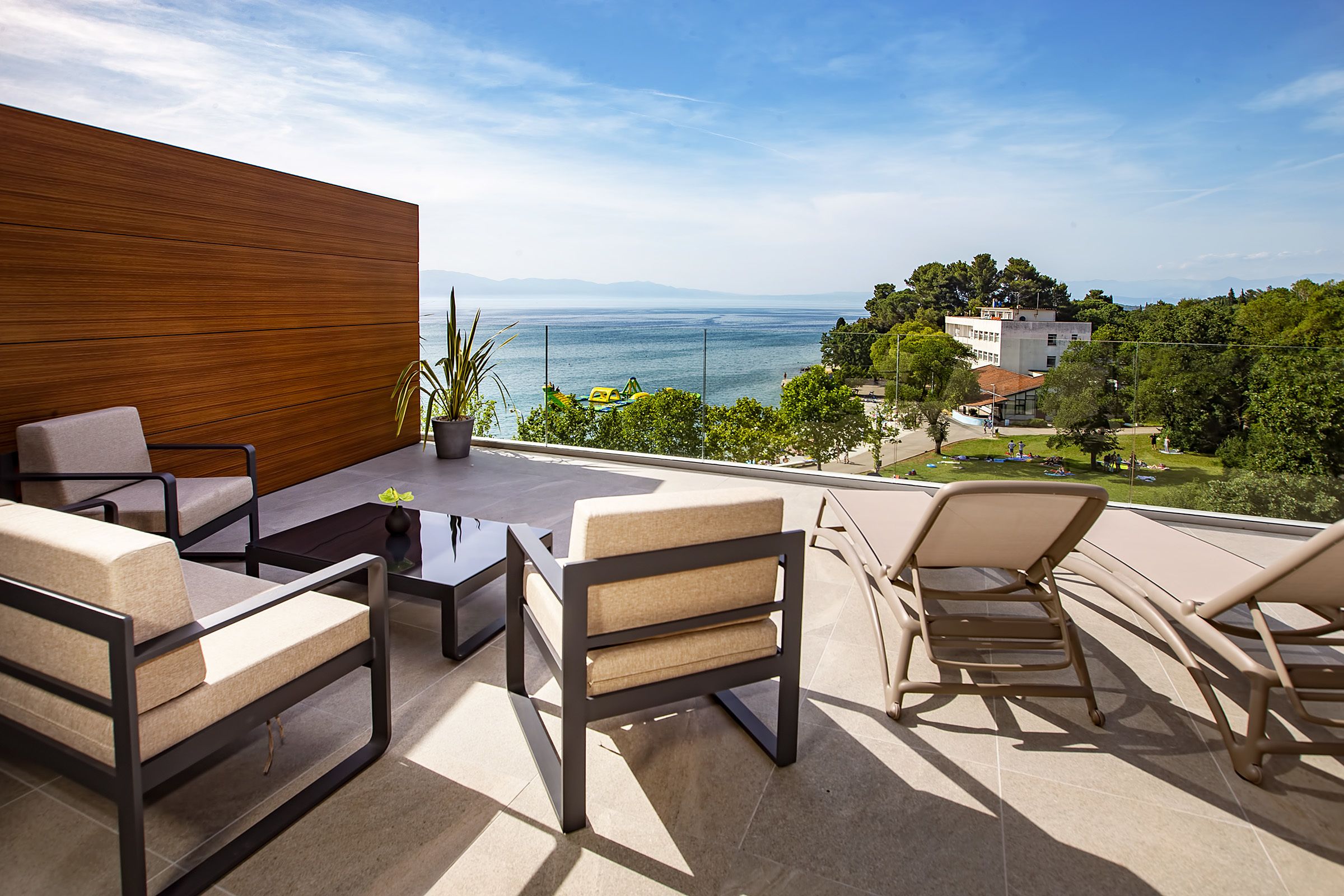 A terrace with outdoor furniture, a view of the sea, and a building in the background.