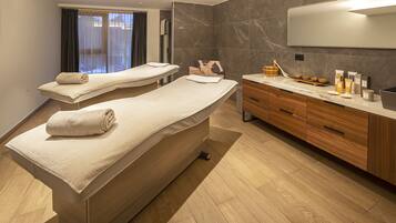 A modern spa room with two massage tables, a wooden vanity, and a large mirror.