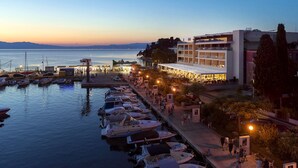 A marina with boats docked, a building with multiple balconies, and a waterfront promenade. - Hotel Riva (Malinska-Dubasnica)