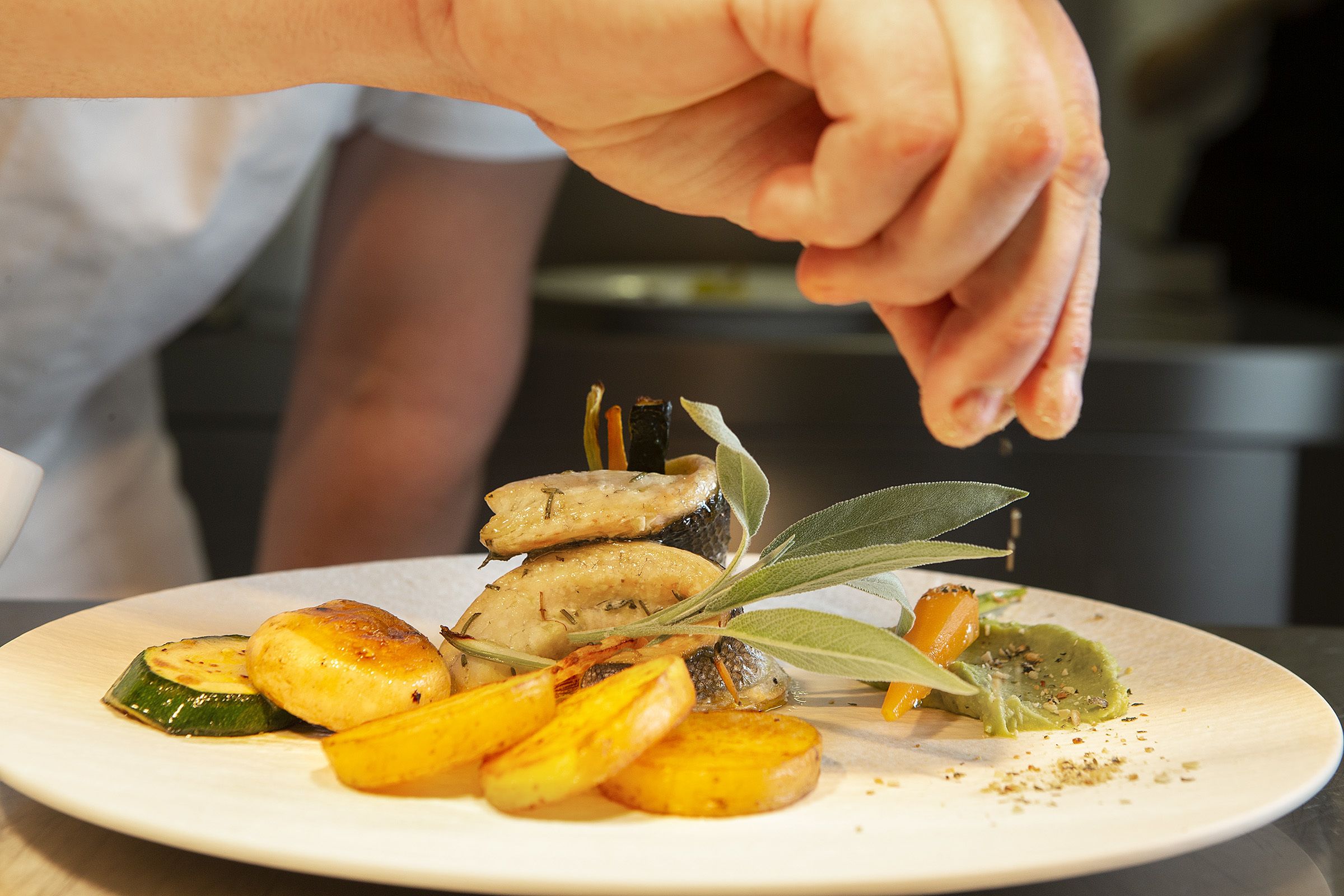 A plate of roasted vegetables with a hand sprinkling seasoning.