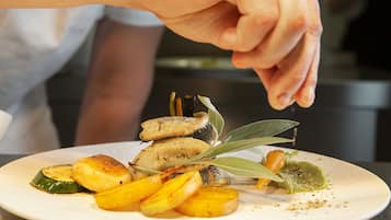 A plate of roasted vegetables with a hand sprinkling seasoning.