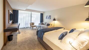 A modern hotel room with a large bed, a desk, a chair, a sofa, and a TV.