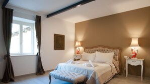 Ein ordentlich eingerichtetes Schlafzimmer mit einem großen Bett, zwei Nachttischen, einer Bank und einem Fenster mit Vorhängen.