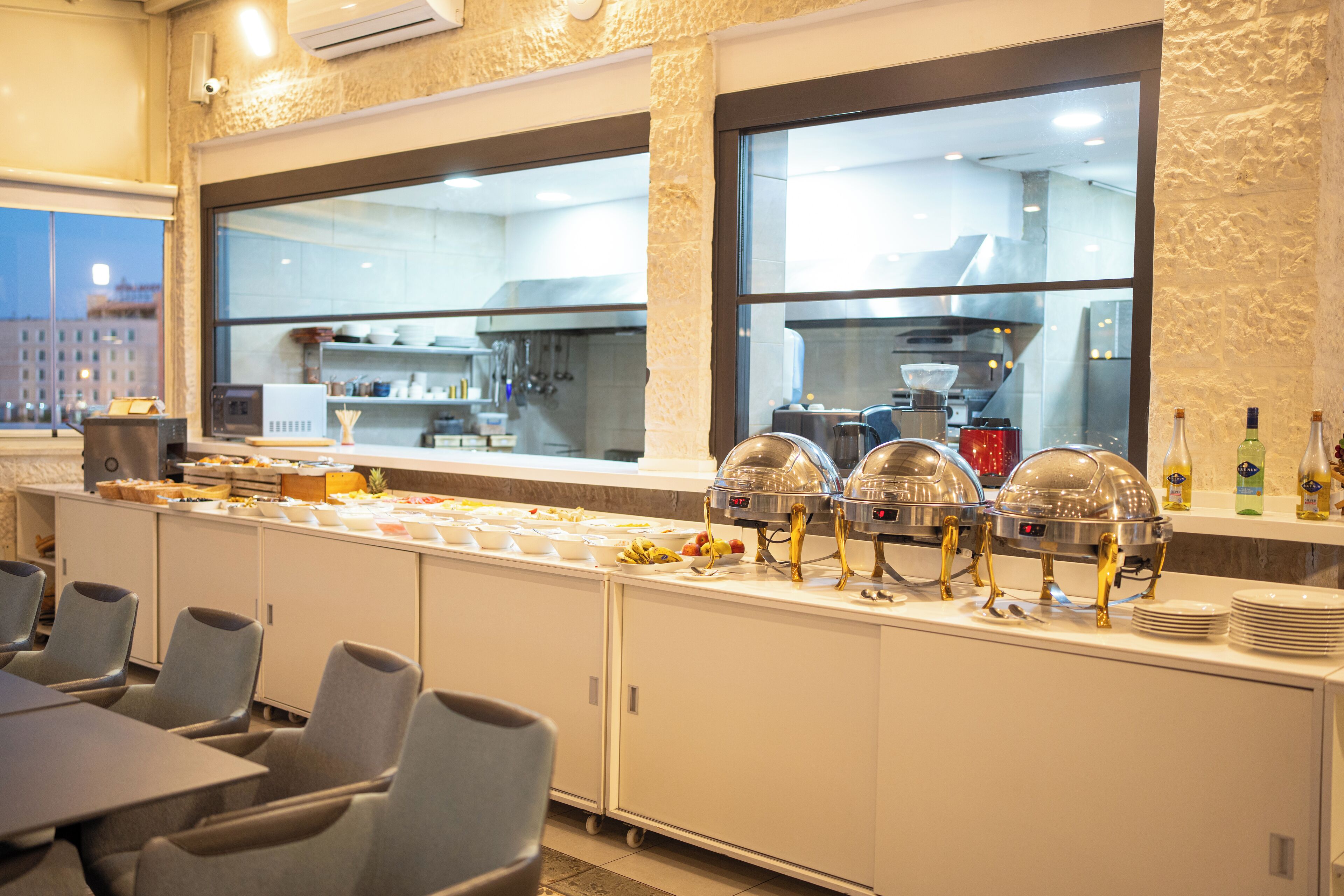Un buffet avec différents postes de service pour la nourriture, un espace pour s’asseoir et une cuisine en arrière-plan.