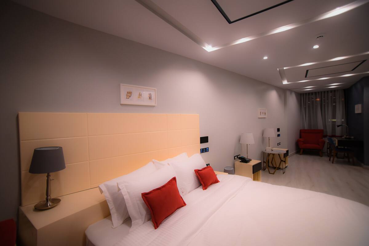 A modern hotel room with a large bed, bedside tables, a desk, and a chair.