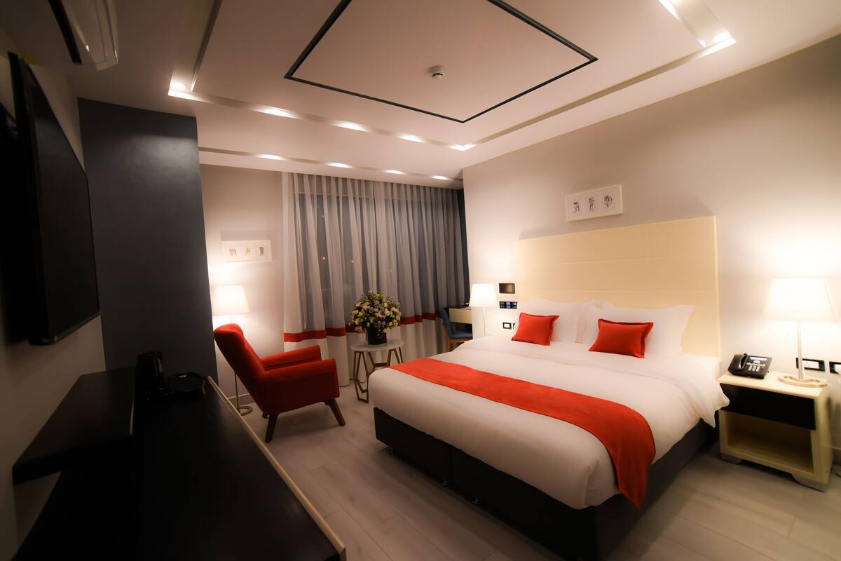 A modern hotel room with a large bed, a desk, a chair, and a TV.