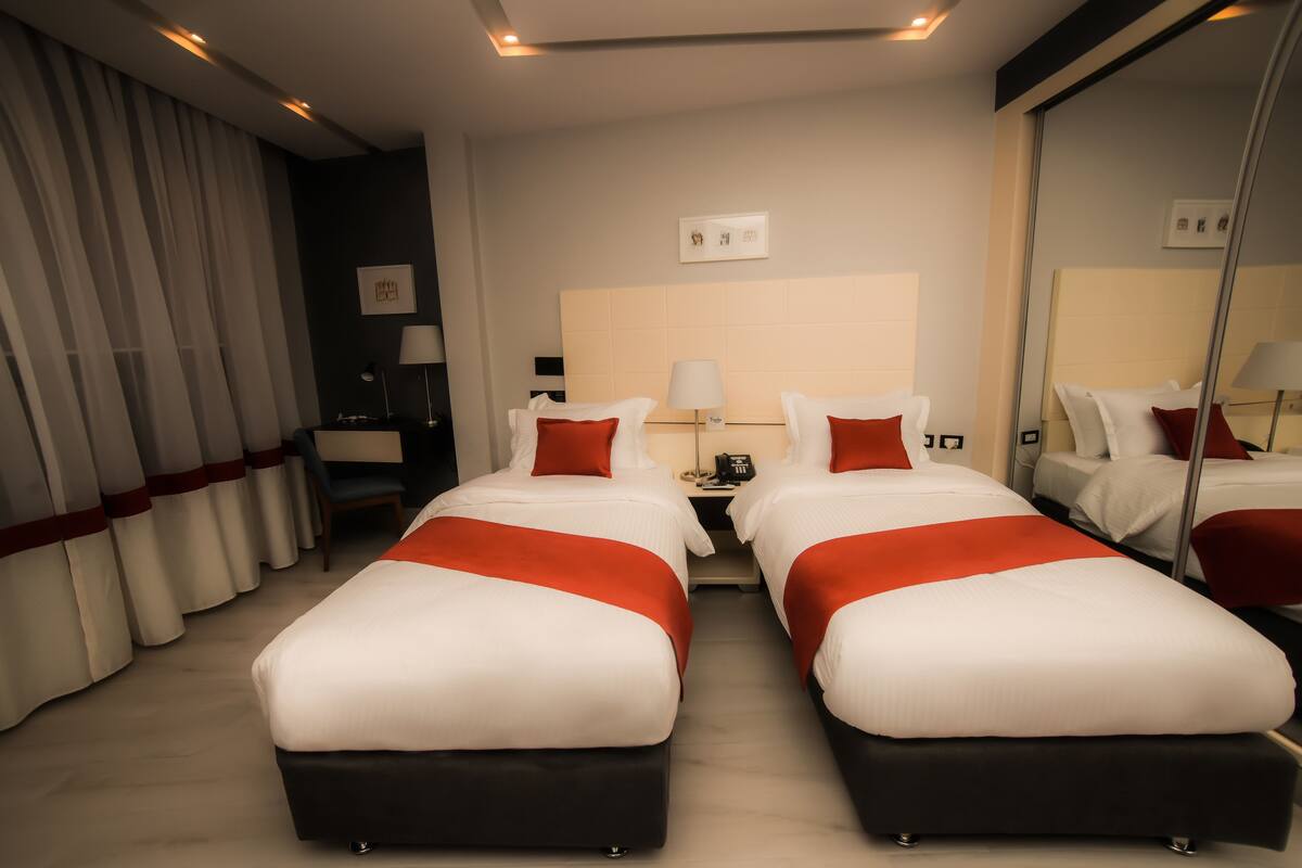 A hotel room with two beds, a nightstand, a desk, and a large mirror.