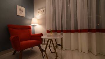 A room with a red armchair, a round table with a vase, and sheer curtains with a red stripe.